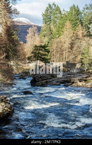 Portrait format: Falls of Dochart looking downstream towards the bridge showing white water, rocks, the bridge, pine trees and mountains in the backgr Stock Photo