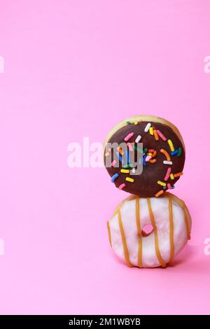 verity Mini-Donuts mit Glasur und Prise auf rosa Hintergrund Stockfoto
