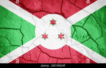 Flagge Burundis. Burundi-Symbol. Flagge auf dem Hintergrund von trockener, gerissener Erde. Burundi-Flagge mit Dürrekonzept Stockfoto