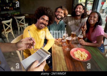Nahaufnahme der Hände eines Kellners, der die Bestellung notiert. Die Gruppe junger Freunde in einer Bar Stockfoto