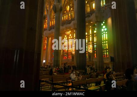 Das Panorama der kathedrale sagrada familia im Inneren wird von natürlichem Sonnenlicht durch Buntglas beleuchtet und einige Menschen beten im Inneren Stockfoto