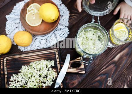 Zerkleinern von Zitrone und schwarzer Holunderbeere auf einem Schneidebrett zur Herstellung eines Kräutergetränks oder eines Medikaments zur Heilung von Sirup aus Holunderblüten zu Hause Stockfoto