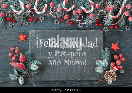 Weihnachtlicher Hintergrund mit Tannenzweigen, roten Beeren und Zuckerstangen mit schwarzem Brett. Feliz Navidad bedeutet "Frohe Weihnachten" auf Spanisch. Stockfoto