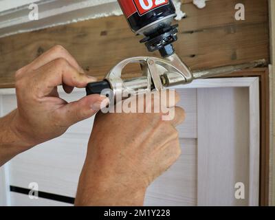 Regelung des Durchflusses von Silikonschaum in der Düse der Baupistole in männlichen Händen bei der Montage des Türrahmens Stockfoto