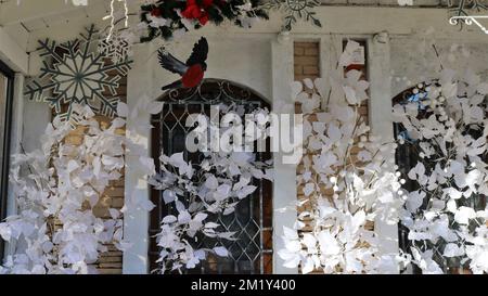 Außendekor aus weißem Material in Form von Blättern, Blumen und Schneeflocken mit einem roten Spritzer eines Winterbullfinkvogel Stockfoto