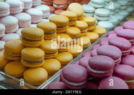 Verschiedene Makronen oder Makronen, die in einem Café ausgestellt werden, französische Wüste, die nach Farben und Aromen gestapelt ist, beliebter süßer Baiser-basierter Keks Stockfoto