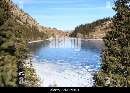 Eisbedeckter Bergsee Kolsai im Winter mit Tannenbäumen bei sonnigem Wetter Stockfoto