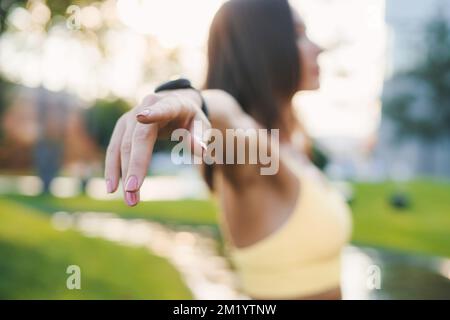 Eine Frau, die im Park Arme streckt und Atemübungen macht. Konzept gesunder Lebensweise und Entspannung. Eine Frau, die Yoga auf dem Rasen praktiziert Stockfoto
