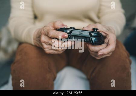 Zugeschnittenes Bild der Hände einer Seniorin, die beim Spielen auf der Spielkonsole den Joystick gedrückt hält und Zeit zu Hause verbringt. Familienheim Freizeit. Ein glücklicher Lebensstil. Stockfoto