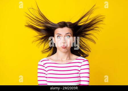 Fotoporträt einer charmanten jungen Frau Wangen aufblasen fliegende Haare Narren Tragen Sie stilvolle gestreifte Kleidung isoliert auf gelbem Hintergrund Stockfoto