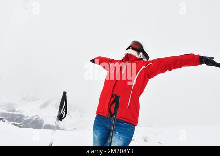 Männliche Person in roter Jacke mit versprühten Händen blickt auf weiße Berge und schneeweiße Gipfel im Hintergrund. Bergumarmungskonzept. Stockfoto