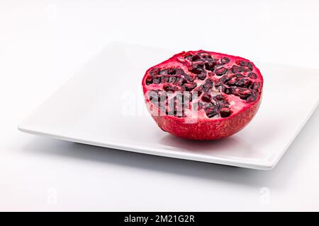 Studioaufnahme eines halben Granatapfel, leuchtend rot belichtet auf einer weißen Platte, ausgeschnitten auf weißem Hintergrund Stockfoto