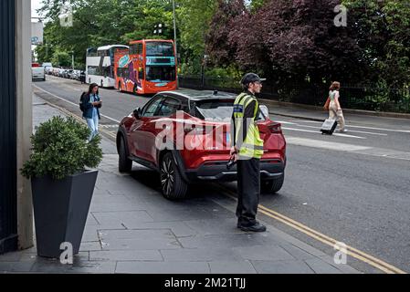 Traffis Warden wartet neben einem Auto, das auf dem Bürgersteig in Edinburgh, Schottland, Großbritannien, geparkt ist. Stockfoto