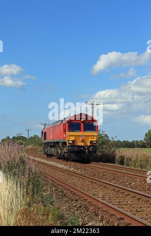 Unter dem weiten blauen Himmel von West Lancashire nähert sich DB Cargo Diesel Lokomotive 66009 einem Fußgängerübergang auf Burscough Moss. Stockfoto