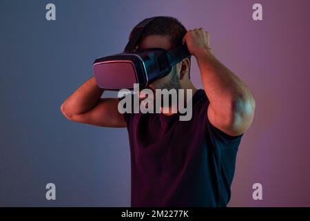 Junger Mann mit VR-Brillen-Headset interagiert mit der virtuellen Realität in Neonfarben, Zukunftstechnologie und Bildungs-Videospielen Stockfoto