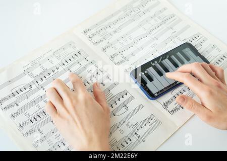 Das Programm am Telefon, um Klavier zu spielen, Klavierergebnis. Musikalische Notizen auf Papier. Das Programm auf dem Smartphone, Übung Stockfoto