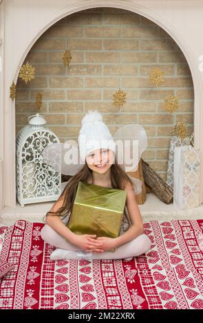 Kleines Mädchen im Feenkostüm pixi hält die Geschenkbox neben dem Weihnachtsbaum. X-Mass und Neujahr Warten und Feiern Konzept. Feiertag-Hure Stockfoto