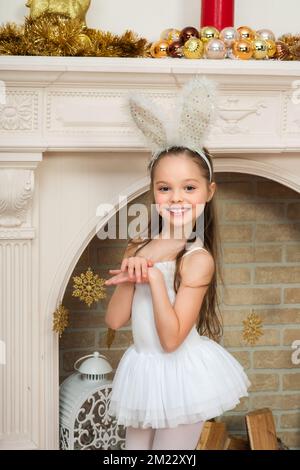 Ein kleines Mädchen im feenkostüm pixi mit Kaninchenohren posiert neben dem Weihnachtsbaum. X-Mass und Neujahr Warten und Feiern Konzept. Ge Stockfoto