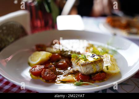 Ein Stück gebackener Lachs, gegrillte Pfeffer, Zitrone und Salz mit trockener Babytomate auf einem ausgefallenen roten Karomuster-Hintergrund in einem Restaurant. Stockfoto