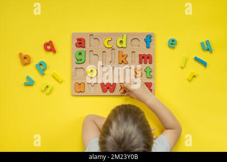 Kindliche Hände halten Alphabet Holzbrett mit farbigen Schriftbuchstaben in Zellen Nahaufnahme isoliert Stockfoto