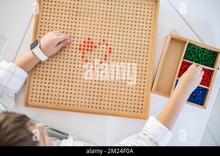 Junge, Kinder, Montessori-Holzbrett mit roten Perlen, Herzform auf dem Schreibtisch Stockfoto