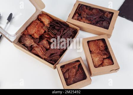 Einige handgefertigte Pappkartons mit dehydrierten Hundefreuden, die höchste ist geöffnet, voller trockenem Fleisch knusprigen Geschmacks von Rind und Huhn. Hausgemachtes Haustier Stockfoto