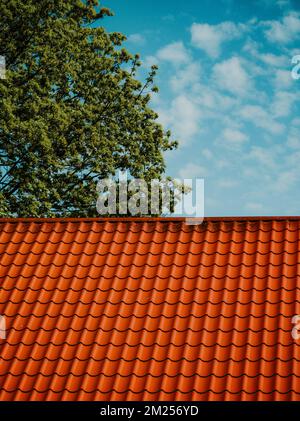 Rot gefliestes Dach. Wolken am blauen Himmel. Grüner Baum. Stockfoto