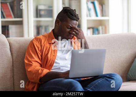 Young upset black man using laptop at home Stockfoto