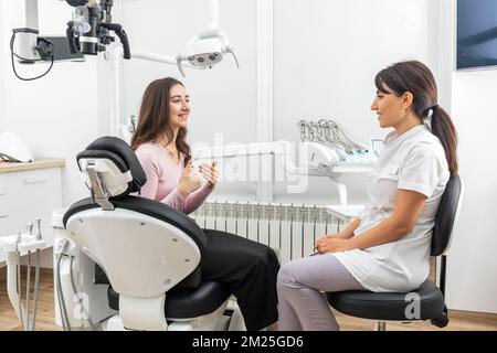 Weibliche Zahnärztin im Gespräch mit einem jungen Patienten während der Verabredung in der modernen Zahnklinik vor der Zahnbehandlung Stockfoto