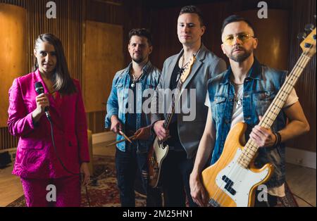 Recording studio interior. Four band members - vocalist, drummer, and two guitarists - stand next to each other and look at camera. . High quality photo Stockfoto