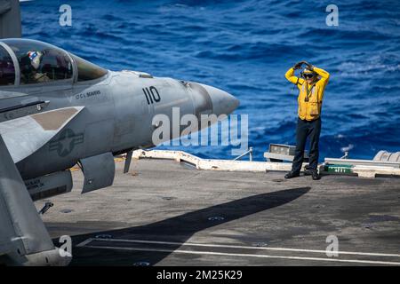 San Diego, Usa. 10. Dezember 2022. EIN US-AMERIKANISCHER Der Navy Deck Handler leitet ein F/A-18F Super Hornet Kampfflugzeug mit den kämpfenden Rothähnen von Strike Fighter Squadron 22 zum Parkplatz auf dem Cockpit des Nimitz-Klasse-Flugzeugträgers USS Nimitz auf dem Pazifik, 10. Dezember 2022 nahe Kalifornien, USA. Kredit: MC1 Nathan Laird/U.S. Navy/Alamy Live News Stockfoto