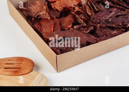 Einige handgefertigte Pappkartons mit dehydrierten Hundefreuden, die höchste ist geöffnet, voller trockenem Fleisch knusprigen Geschmacks von Rind und Huhn. Hausgemachtes Haustier Stockfoto