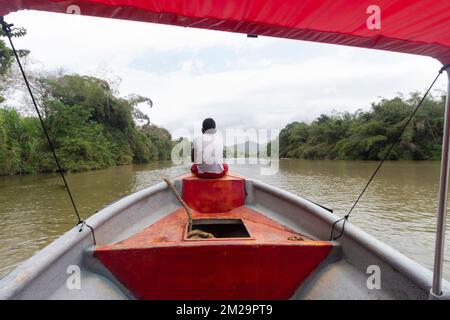 Ein Junge sitzt auf einem Boot und beobachtet die kolumbianische palomino-Flusslandschaft und die berge der sierra nevada an bewölkten Tagen Stockfoto