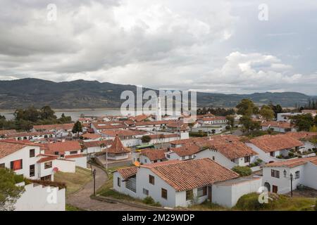 Guatavita kolumbianische Stadt mit weißer Struktur, roten Keramikdächern und andenbergen und tomin-See im Hintergrund am Abend. Stockfoto