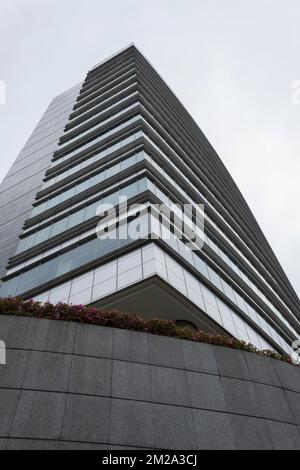 Niedriger Winkel mit Blick auf einen modernen grauen Wolkenkratzer mit kleinem Blumengarten und grauem Himmel Stockfoto