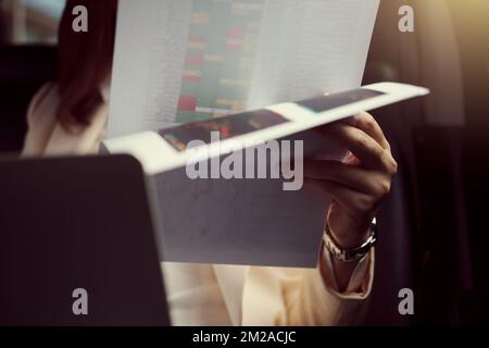 Junge Geschäftsfrau, die auf dem Rücksitz des Autos sitzt und Papierkram in der Hand liest. Stockfoto