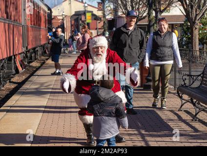 December 11, 2022: Strasburg, Pennsylvania: Parents watch as Senior Gentlemen dressed as Santa Claus greets small child at Strasburg Railroad Christma Stock Photo