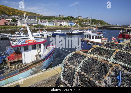 Stacked lobster creels / traps on quay and fishing boats in the harbour of Helmsdale, Sutherland, Scottish Highlands, Scotland, UK | Casiers à homards / nasses et bateaux de pêche au port de Helmsdale, Sutherland, Ecosse, Royaume-Uni 26/05/2017 Stock Photo