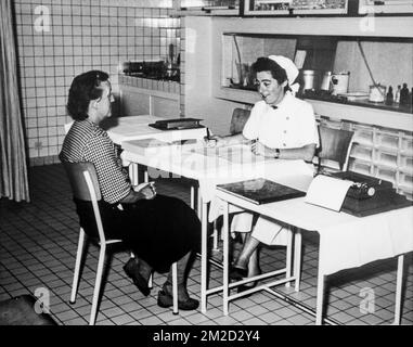 Old black and white archival photograph showing female factory worker visiting nurse at dispensary in the 1950s | Vieille photo d'une infirmière examinant une ouvrière dans infirmerie d'usine pendant les années cinquante 11/02/2018 Stock Photo
