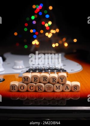 Wooden blocks with the inscription Merry Rock Mas on an old used vintage guitar with colorful Christmas lights bokeh background Stock Photo