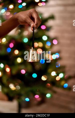 Girl holding a Christmas bell in front of a blurred out background of a Christmas tree lights. Stockfoto