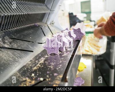 bäckermeister schneidet in der Gastronomieküche rote violettgelbe und grüne Sterne und herzförmige Buns Stockfoto