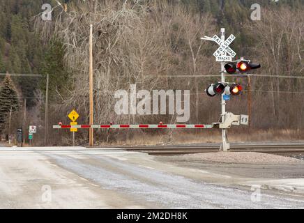 Troy, Montana, USA. 23. Februar 2021. Rote Warnblinkleuchten und ein unteres Tor am Bahnübergang 3.. Straße, Troy, Montana. Stockfoto