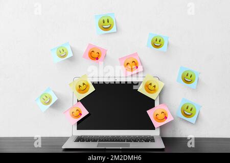 Modern laptop and different sticky note papers with drawn emoticons on light background Stock Photo
