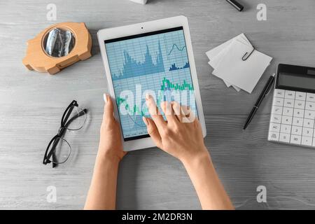 Woman holding tablet computer with stock data on grey wooden background. Finance trading Stock Photo