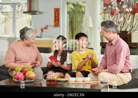 Großeltern geben ihrem Enkel und ihrer Enkelin rote Glückssumschläge Stockfoto