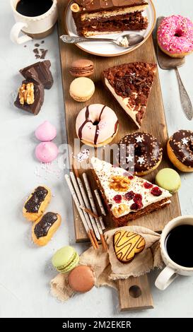 Auswahl an verschiedenen Kuchenstücken, Makronen, Baiser, Kekse und Donuts auf einem Holztisch mit hellem Hintergrund. Draufsicht. Hintergrund für Süßwaren. Stockfoto