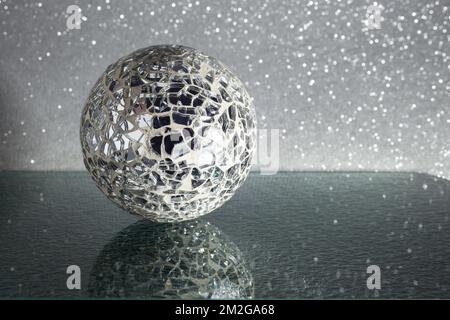 Zerdrückte Spiegelmosaikkkugel auf schwarzem Glas mit Reflexionen und silbernem Glitzerhintergrund Stockfoto