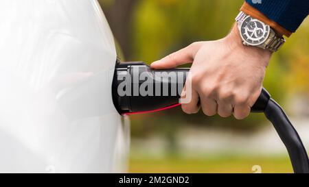 Nahansicht eines Mannes, der das Ladegerät an einen Ladeanschluss für Elektroautos anschließt Stockfoto
