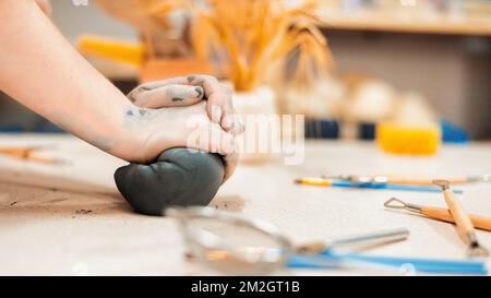 Der Meister der Töpferkunst, der in einem Studio arbeitet. Sie knete ein Stück Lehm mit ihren Händen. Werkzeuge auf dem Tisch Stockfoto